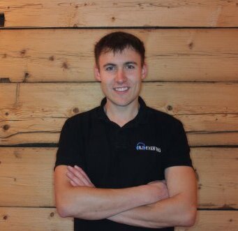 Nico Japes, professioneller Hochzeits-DJ und Inhaber von NJ-Eventing aus Kirchhundem. Er lächelt im Marken-Shirt vor einer Holzwand. Ihr Experte für Eventtechnik im Kreis Olpe und Sauerland.